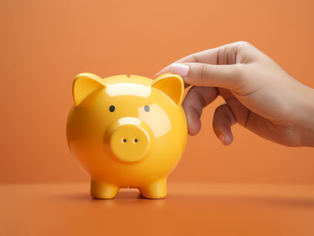 Piggy bank in female hand on orange background with copy spaceの素材