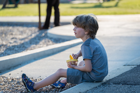 Portrait of a little boy sitting on a curb in parkの写真素材
