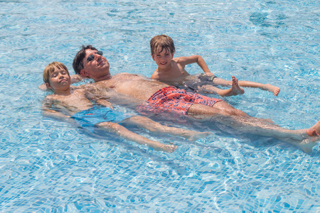Father and his boys laying in a poolの写真素材