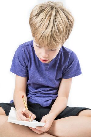 Portrait of a boy sitting and writing on a piece of paper, isolated on a white backgroundの写真素材