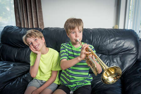 Two kids sitting on a sofa. 
One is playing a trumpet and the other child is listening and smiling.の写真素材