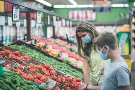 Chicago,IL- August 21, 2021:Mother and  child wearing masks shopping at supermarket for editorial use only Family wearing masks picking fresh veggies / fruits at supermarket- pandemic conceptのeditorial素材