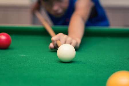 Cute boy in blue t shirt plays billiard or pool in club. Young Kid learns to play snooker. Boy with billiard cue strikes the ball on table. Active Leisure, sport, hobby conceptの写真素材