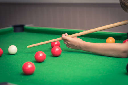 Cute boy in blue t shirt plays billiard or pool in club. Young Kid learns to play snooker. Boy with billiard cue strikes the ball on table. Active Leisure, sport, hobby conceptの写真素材