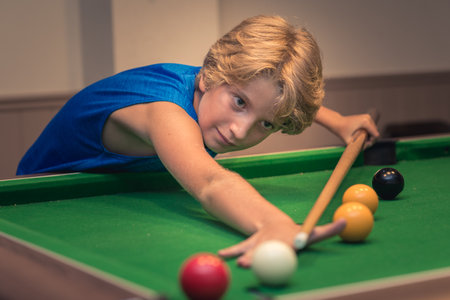 Cute boy in blue t shirt plays billiard or pool in club. Young Kid learns to play snooker. Boy with billiard cue strikes the ball on table. Active Leisure, sport, hobby conceptの写真素材