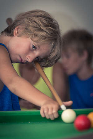 Cute boy in blue t shirt plays billiard or pool in club. Young Kid learns to play snooker. Boy with billiard cue strikes the ball on table. Active Leisure, sport, hobby conceptの写真素材