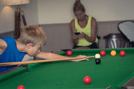 Cute boy in blue t shirt plays billiard or pool in club. Young Kid learns to play snooker. Boy with billiard cue strikes the ball on table. Active Leisure, sport, hobby conceptの写真素材