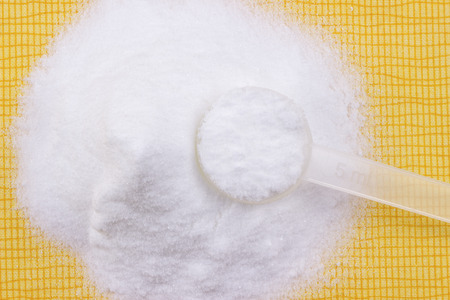 Creatine monohydrate powder and measure spoon on a yellow tablecloth.の写真素材