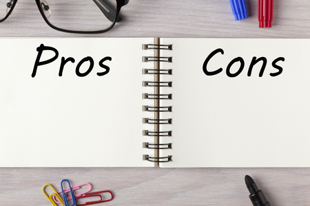 Pros and Cons List written in notebook on wooden desk with marker pen and glasses. Top view.の写真素材