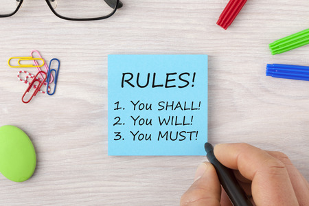 Hand writing RULES! You SHALL! You WILL! You MUST! in note with marker pen and glasses on wooden desk. Business Concept. Top view.の写真素材
