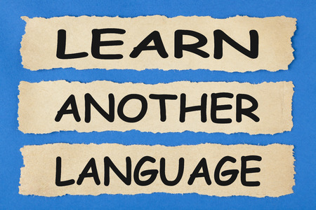 LEARN ANOTHER LANGUAGE written on old torn paper on blue background. Business concept. の写真素材