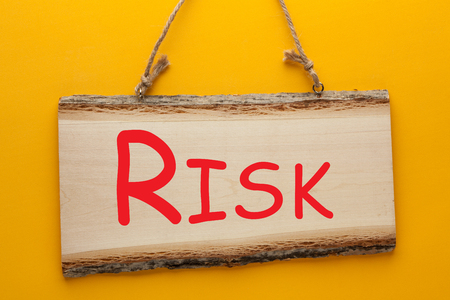 Risk word on wooden sign hanging on a rope on yellow background. Business conceptの写真素材