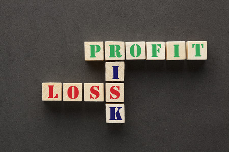 Risk, profit and loss crossword puzzle on cubes shape wooden blocks on black background. Business Concept.の写真素材