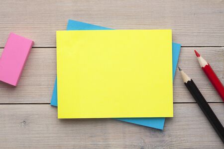 Yellow note with empty place for your text with pencil and eraser aside on wooden desk. Reminder...