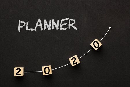 Planner 2020 concept with directional arrow written on cubes shape wooden blocks on black background.の写真素材