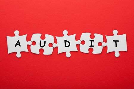 Audit word in pieces paper puzzle on red background. Business concept.の写真素材