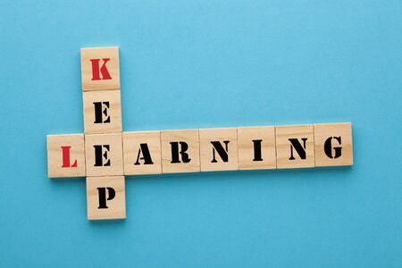 Words keep learning concept crossword clues in wooden blocks on blue background.