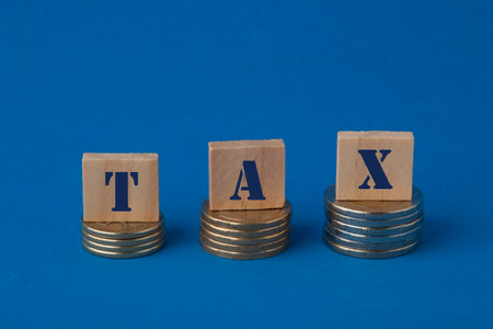 Tax concept with wooden block on step stacked coins on blue background. Business and finance...