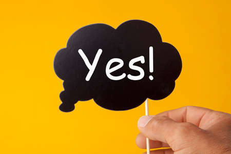 Hand holding speech bubble with word yes.