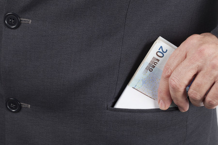 Man in suit putting a wad of twenty Euros banknotes in his pocket.の写真素材