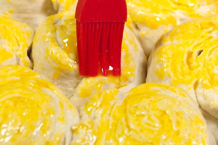 Spreading a yellow egg glaze on handmade bread by brush before baking. . の写真素材