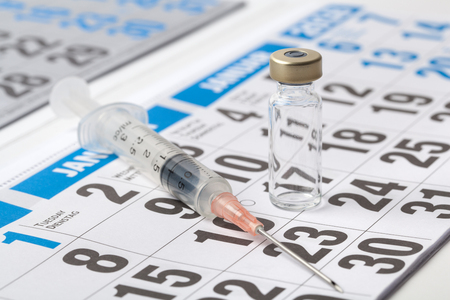 Transparent vial ampoule of a vaccine and syringe on a sheet of calendarの写真素材