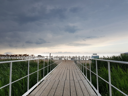Wooden bridge as trail to the beach in a cloudy summer day before rain.の写真素材