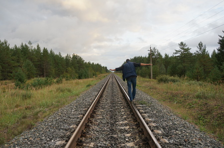 A young man walks along the rails in the forest zone. View from the back