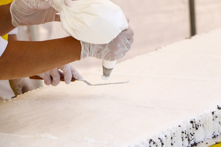 Confectioner decorating tasty cupcake with butter cream.  confectioner's hands in white gloves put  white cream of whipped cream on large festive cake sponge cake.の写真素材