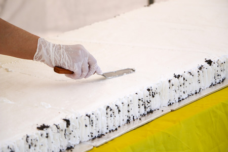 Confectioner decorating tasty cupcake with butter cream.  confectioner's hands in white gloves put  white cream of whipped cream on large festive cake sponge cake.の写真素材