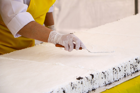 Confectioner decorating tasty cupcake with butter cream.  confectioner's hands in white gloves put  white cream of whipped cream on large festive cake sponge cake.の写真素材