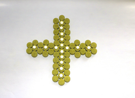 cross made of green pills on white background. medical preparations. medicine from natural plants.の写真素材