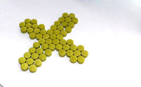 cross made of green pills on white background. medical preparations. medicine from natural plants.の写真素材