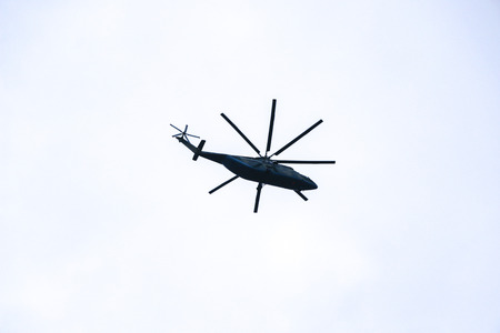 large military helicopter hovers in  sky. A camouflaged helicopter flies at high speed.