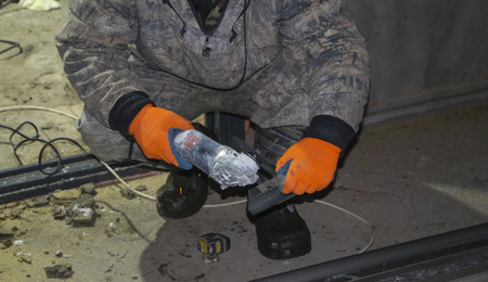 The hands of the worker in gloves cut metal profile with a grinding machine. orange sparks fly from...