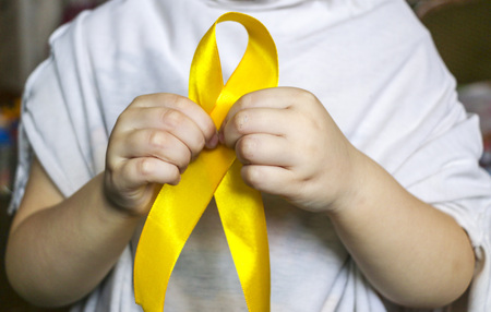 golden ribbon  in the hands of a child. Concept: pediatric oncology, children's cancer.の写真素材