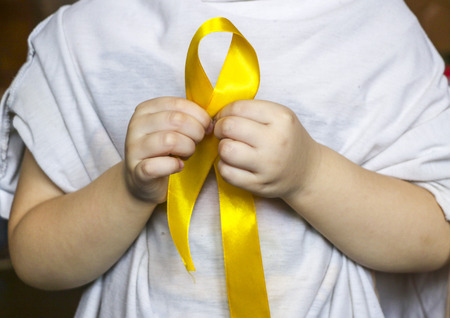 golden ribbon  in the hands of a child. Concept: pediatric oncology, children's cancer.の写真素材