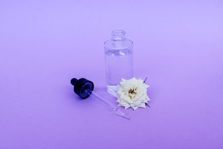 Glass bottle with oil or serum pipette, with small white rose flower on delicate background. Concept: organic bio cosmetics, vegetable oils, serum collagen, skin careの写真素材