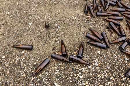 whole and broken brown bottles are scattered on the gravel.Concept: waste recycling, disposal of...