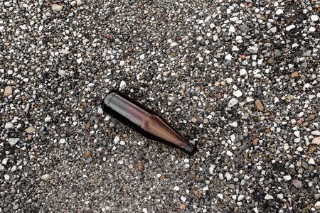 whole and broken brown bottles are scattered on the gravel.Concept: waste recycling, disposal of...
