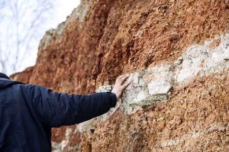A young man walks in the clay career in winter. The guy touches his hands with multi-colored layers of clay in the excavation.の写真素材