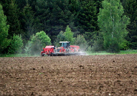 A large tractor with a plow plows a field before the spring sowing of crops. A tractor with a harrow...