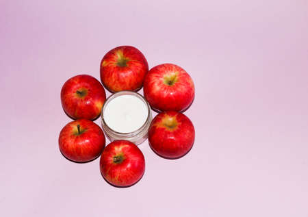 cosmetic composition with red ripe juicy apples, and an open jar with a white gentle moisturizing...