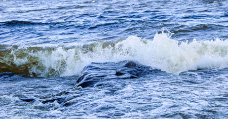 waves run onto shore and crash against the rocks, creating many splashes and splashes near shore....