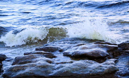 waves run onto shore and crash against the rocks, creating many splashes and splashes near shore....