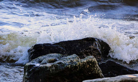 waves run onto shore and crash against the rocks, creating many splashes and splashes near shore....