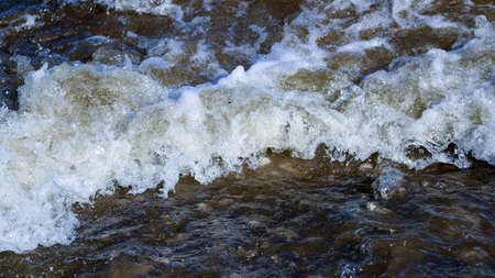 waves run onto the shore and crash against the rocks, creating many splashes and splashes near the shore. river surf in stormy weather near a stone pebble coast with foamy splashing waves.の写真素材