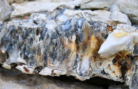 Diverse colored quartz rock in cut of earth. Deposits of gray, white, orange quartz. Untreated semi-precious stones of the chalcedony variety in various stone deposits and layers of different rocks.の写真素材