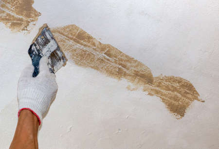 mans hand in a cloth glove with a spatula and putty, applies mastic to wall, ceiling to level...