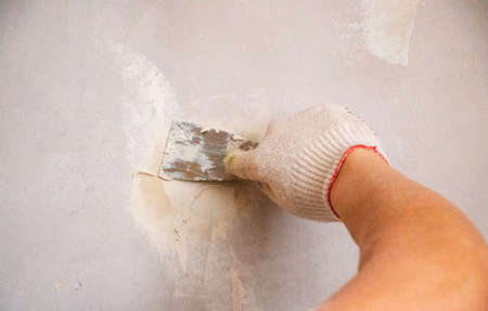 mans hand in a cloth glove with a spatula and putty, applies mastic to wall, ceiling to level surface. process of applying mastic with a spatula to surface for interior design of the room.の写真素材